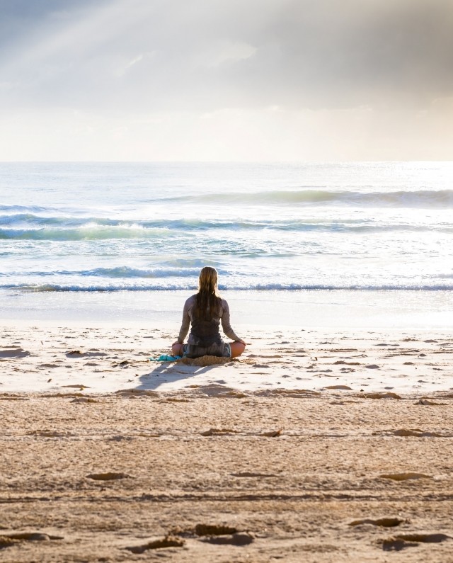 A woman is meditating on a beach