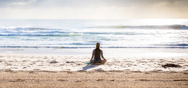 A woman is meditating on a beach